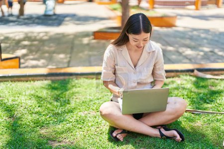 Téléchargez les photos : Femme chinoise utilisant un ordinateur portable assis sur l'herbe au parc - en image libre de droit