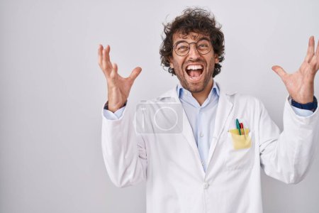 Photo for Hispanic young man wearing doctor uniform celebrating crazy and amazed for success with arms raised and open eyes screaming excited. winner concept - Royalty Free Image