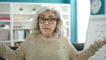 Téléchargez les photos : Femme d'âge moyen avec professeur de cheveux gris debout avec je ne sais quelle expression à l'université - en image libre de droit