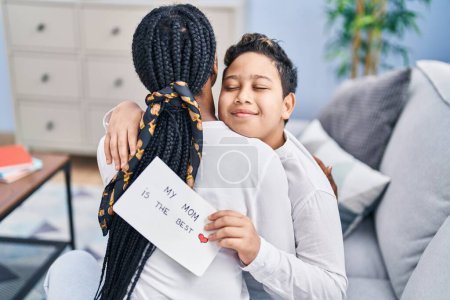 Téléchargez les photos : Afro-américaine mère et fils étreignant l'autre tenant beau papier de message à la maison - en image libre de droit