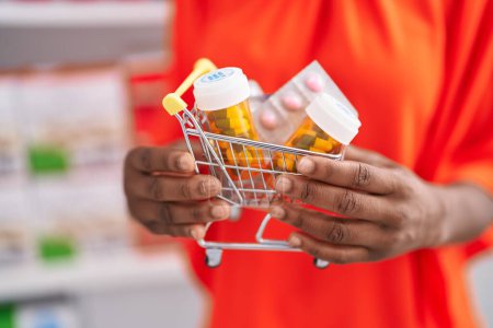 Photo for African american woman customer holding market cart with pills at pharmacy - Royalty Free Image