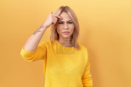 Téléchargez les photos : Jeune femme caucasienne portant un pull jaune pointant malheureux à boutons sur le front, infection laide de la tête noire. acné et problème de peau - en image libre de droit