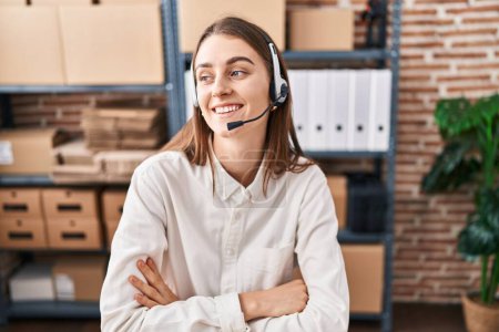 Photo for Young caucasian woman working at small business ecommerce wearing headset looking away to side with smile on face, natural expression. laughing confident. - Royalty Free Image