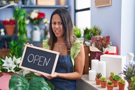 Photo for Hispanic young woman working at florist with open sign clueless and confused expression. doubt concept. - Royalty Free Image