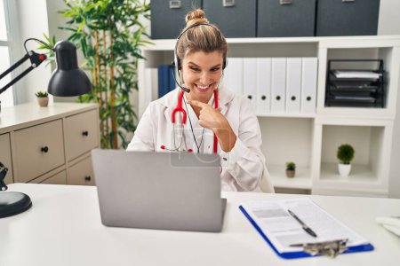 Téléchargez les photos : Jeune femme médecin portant uniforme de médecin travaillant à l'aide d'un ordinateur portable souriant heureux pointant avec la main et le doigt - en image libre de droit