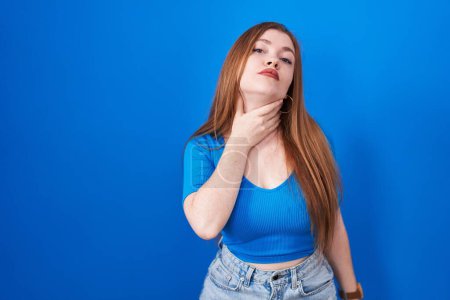 Photo for Redhead woman standing over blue background touching painful neck, sore throat for flu, clod and infection - Royalty Free Image