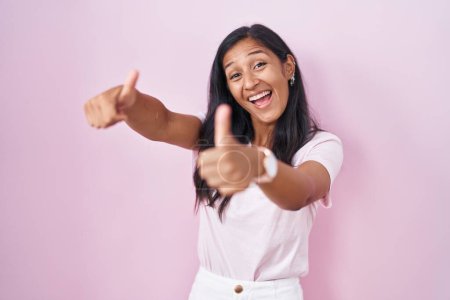 Photo for Young hispanic woman standing over pink background approving doing positive gesture with hand, thumbs up smiling and happy for success. winner gesture. - Royalty Free Image