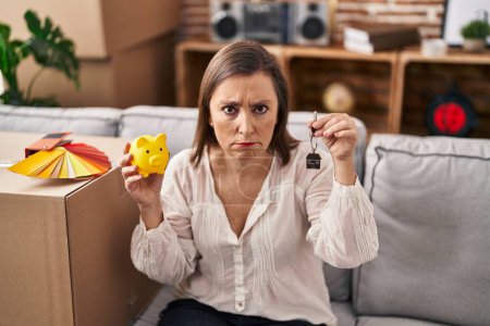 Photo for Middle age hispanic woman holding piggy bank at new home skeptic and nervous, frowning upset because of problem. negative person. - Royalty Free Image