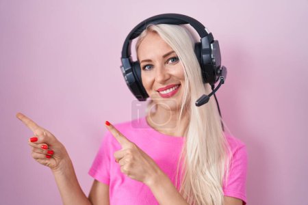 Photo for Caucasian woman listening to music using headphones smiling and looking at the camera pointing with two hands and fingers to the side. - Royalty Free Image