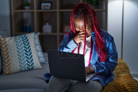 Photo for African american woman with braided hair using computer laptop at night laughing and embarrassed giggle covering mouth with hands, gossip and scandal concept - Royalty Free Image