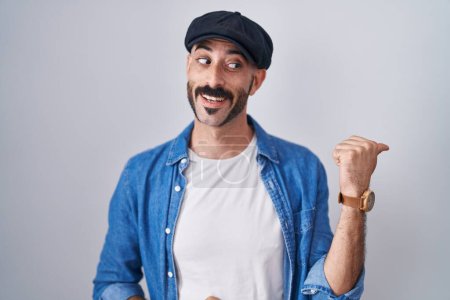 Téléchargez les photos : Homme hispanique avec la barbe debout sur fond isolé souriant avec le visage heureux regardant et pointant vers le côté avec le pouce vers le haut. - en image libre de droit