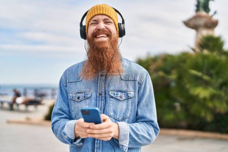 Foto de Young redhead man smiling confident listening to music at street - Imagen libre de derechos