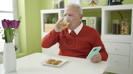 Téléchargez les photos : Seniors manger des cookies et boire du jus en utilisant un smartphone à la maison - en image libre de droit