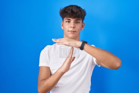 Photo for Hispanic teenager standing over blue background doing time out gesture with hands, frustrated and serious face - Royalty Free Image