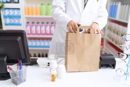 Photo for Non binary man pharmacist putting products on shopping bag at pharmacy - Royalty Free Image