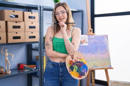 Photo for Young woman artist holding paintbrush and palette at art studio - Royalty Free Image