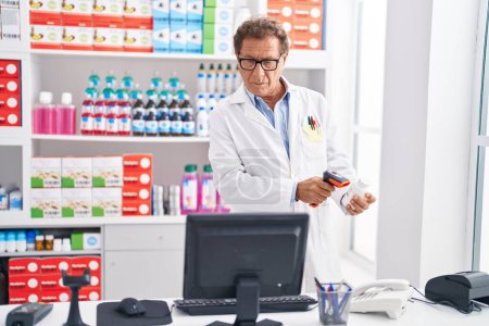 Foto de Hombre de mediana edad farmacéutico escaneo píldoras botella en la farmacia - Imagen libre de derechos