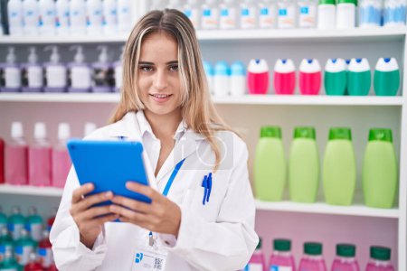 Téléchargez les photos : Young blonde woman pharmacist using touchpad working at pharmacy - en image libre de droit
