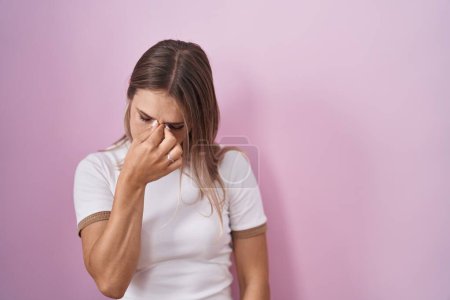 Foto de Blonde caucasian woman standing over pink background tired rubbing nose and eyes feeling fatigue and headache. stress and frustration concept. - Imagen libre de derechos