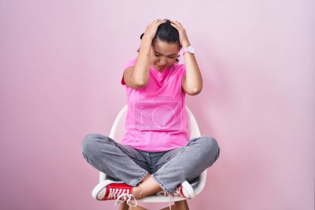 Photo for Hispanic young woman sitting on chair over pink background suffering from headache desperate and stressed because pain and migraine. hands on head. - Royalty Free Image