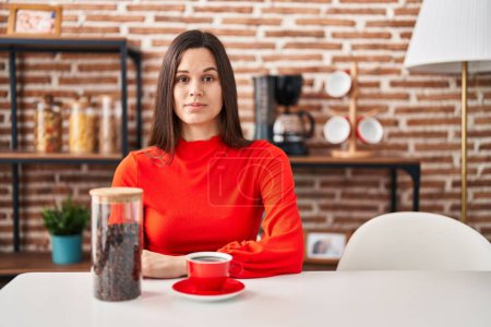 Foto de Joven mujer hispana bebiendo café en casa pensando actitud y expresión sobria buscando confianza en sí misma - Imagen libre de derechos