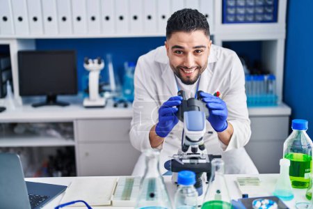 Téléchargez les photos : Jeune homme arabe scientifique utilisant un microscope travaillant en laboratoire - en image libre de droit
