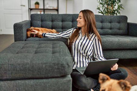 Téléchargez les photos : Jeune femme hispanique utilisant un ordinateur portable assis sur le sol avec des chiens à la maison - en image libre de droit