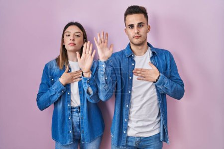 Téléchargez les photos : Jeune couple hispanique debout sur fond rose jurant avec la main sur la poitrine et la paume ouverte, faisant un serment de fidélité - en image libre de droit