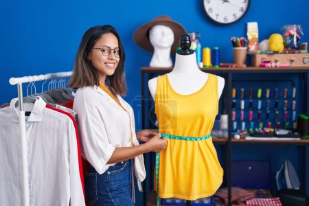 Téléchargez les photos : Jeune femme hispanique tailleur souriant confiant t-shirt mesure au studio de couture - en image libre de droit