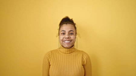 Téléchargez les photos : Jeune femme afro-américaine souriante confiante sur fond jaune isolé - en image libre de droit