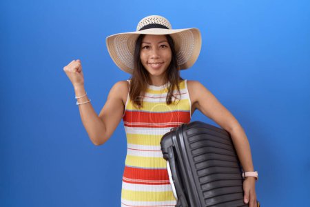 Foto de Mujer china de mediana edad sosteniendo la maleta que va de vacaciones de verano gritando orgulloso, celebrando la victoria y el éxito muy emocionado con los brazos levantados - Imagen libre de derechos