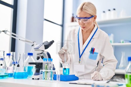 Photo for Young blonde woman wearing scientist uniform measuring liquid at laboratory - Royalty Free Image