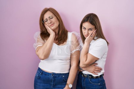 Téléchargez les photos : Mère et fille hispaniques portant un t-shirt blanc décontracté sur fond rose pensant fatigué et ennuyé par des problèmes de dépression avec les bras croisés. - en image libre de droit