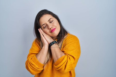 Foto de Young hispanic woman standing over isolated background sleeping tired dreaming and posing with hands together while smiling with closed eyes. - Imagen libre de derechos