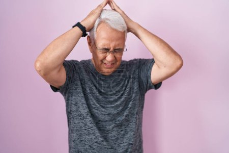 Photo for Middle age man with grey hair standing over pink background suffering from headache desperate and stressed because pain and migraine. hands on head. - Royalty Free Image