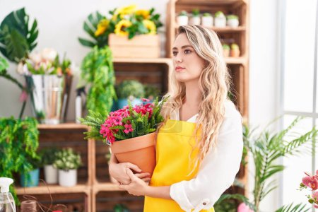 Téléchargez les photos : Young blonde woman florist holding plant at florist - en image libre de droit
