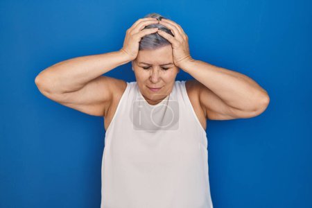 Photo for Middle age caucasian woman standing over blue background suffering from headache desperate and stressed because pain and migraine. hands on head. - Royalty Free Image