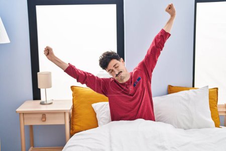 Foto de Young caucasian man waking up stretching arms at bedroom - Imagen libre de derechos