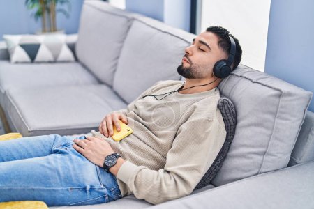 Téléchargez les photos : Jeune homme arabe écoutant de la musique dormir sur le canapé à la maison - en image libre de droit