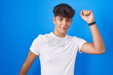 Photo for Hispanic teenager standing over blue background dancing happy and cheerful, smiling moving casual and confident listening to music - Royalty Free Image