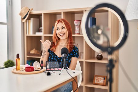 Photo for Young caucasian woman applying make up doing tutorial smiling with happy face looking and pointing to the side with thumb up. - Royalty Free Image