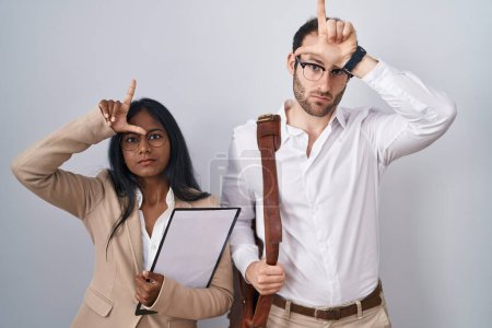 Téléchargez les photos : Couple d'affaires Interracial portant des lunettes se moquant des gens avec les doigts sur le front faisant geste perdant moquerie et insultant. - en image libre de droit