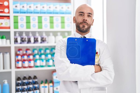 Téléchargez les photos : Jeune homme chauve pharmacien tenant presse-papiers à la pharmacie - en image libre de droit