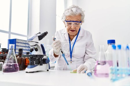 Photo for Senior grey-haired woman wearing scientist uniform using pipette at laboratory - Royalty Free Image