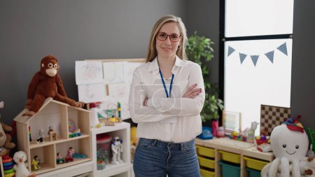 Photo for Young blonde woman preschool teacher smiling confident standing with arms crossed gesture at kindergarten - Royalty Free Image