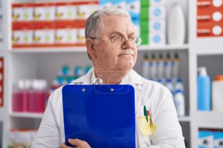 Téléchargez les photos : Middle age grey-haired man pharmacist holding clipboard at pharmacy - en image libre de droit
