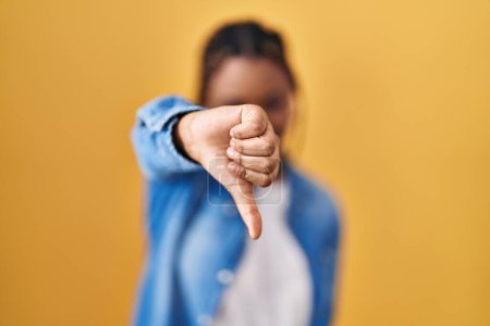Photo for African american woman with braids standing over yellow background looking unhappy and angry showing rejection and negative with thumbs down gesture. bad expression. - Royalty Free Image