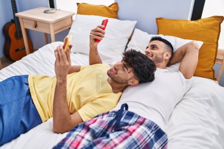 Foto de Dos hombre pareja usando teléfono inteligente acostado en la cama en el dormitorio - Imagen libre de derechos