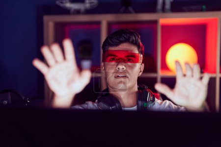 Photo for Young hispanic man streamer playing video game using virtual reality glasses at gaming room - Royalty Free Image