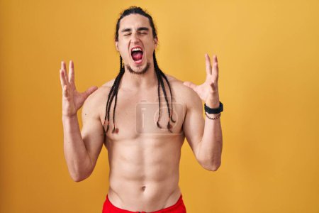 Photo for Hispanic man with long hair standing shirtless over yellow background celebrating mad and crazy for success with arms raised and closed eyes screaming excited. winner concept - Royalty Free Image
